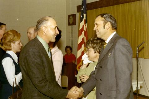 Frank Denholm greeting a man at an event. Millie Denholm is standing to the left of him greeting people.