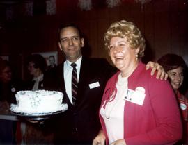 Frank Denholm holding cake in one hand for Donna Kuhfeldwho is standing next to him. She is wearing a McGovern button on her lapel.