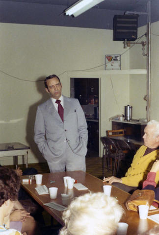 Frank Denholm standing at the head of a table talking to people seated at the table