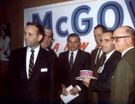 Frank Denholm with a group of men at a South Dakota Democratic Party campaign rally. They are standing in front of a McGovern sign. One man is holding a hat with McGovern printed on it.