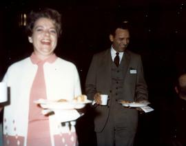 Frank and Millie Denholm at a campaign event. They are carrying plates of food and have drinks in their hands.
