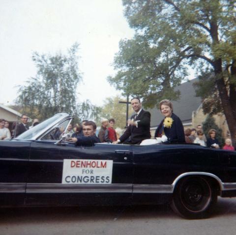 Frank Denholm and his wife, Millie, are in a parade riding in the back of a convertible.