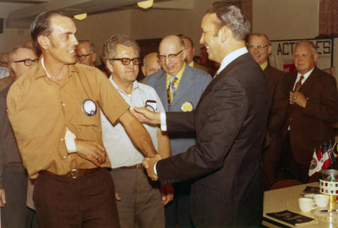 Frank Denholm is shaking hands with constituents at a Kiwanis Club meeting.